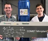 Zu sehen sind zwei Forscher, die ein Schema zeigen, wie Oxymethylenether als Dieselersatz hergestellt wird.