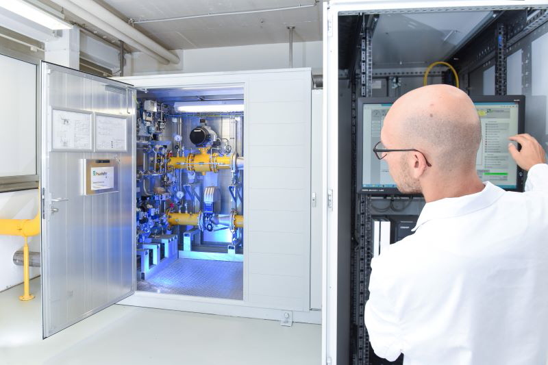 Ein Forscher im weißen Kittel blickt im Labor in einer Wasserstoff-Pilotanlage