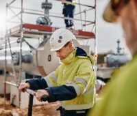 Zwei Arbeiter mit Schutzhelm und -weste am Standort einer Gaspipeline.