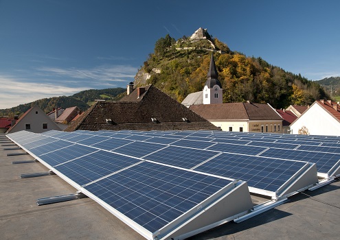 Foto einer PV-Anlage auf einem Flachdach. Im Hintergrund ein Österreichisches Dorf und Berge.