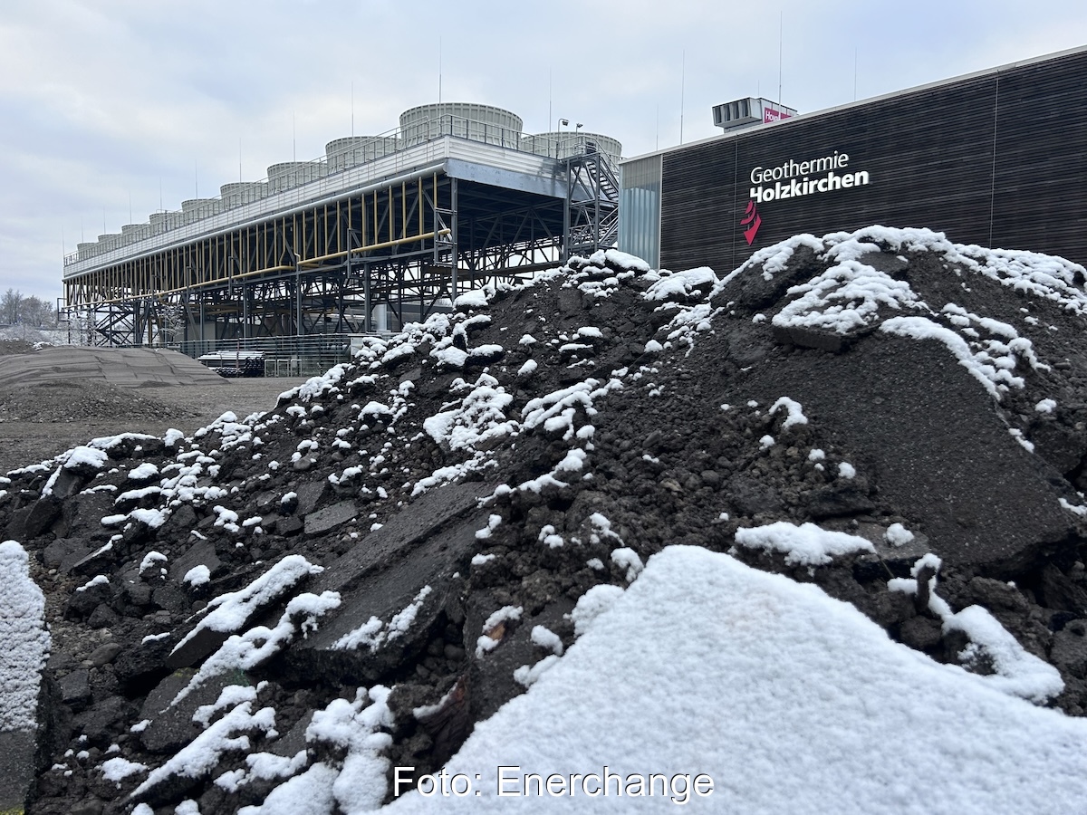 Dunkler Erdhaufen mit etwas Schnee, im Hintergrund ein Gebäude mit der Aufschrift "Geothermie Holzkirchen"