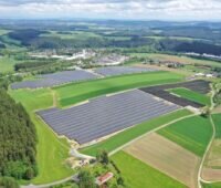 Luftbild zeigt mehrere Solarparks umgeben von Wiesen, Feldern und einer nahen Ortschaft.