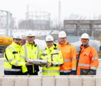 Drei Männer in Signaljacken bei der Grundsteinlegung.