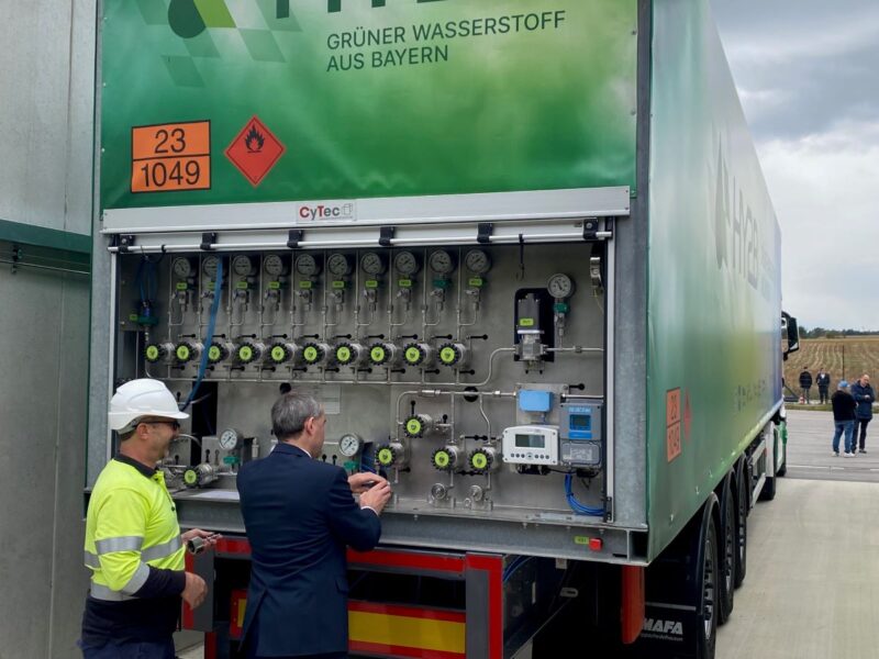 Zwei Personen hantzieren an einem LKW mit der Aufschrift grüner Wasserstoff aus Bayern.