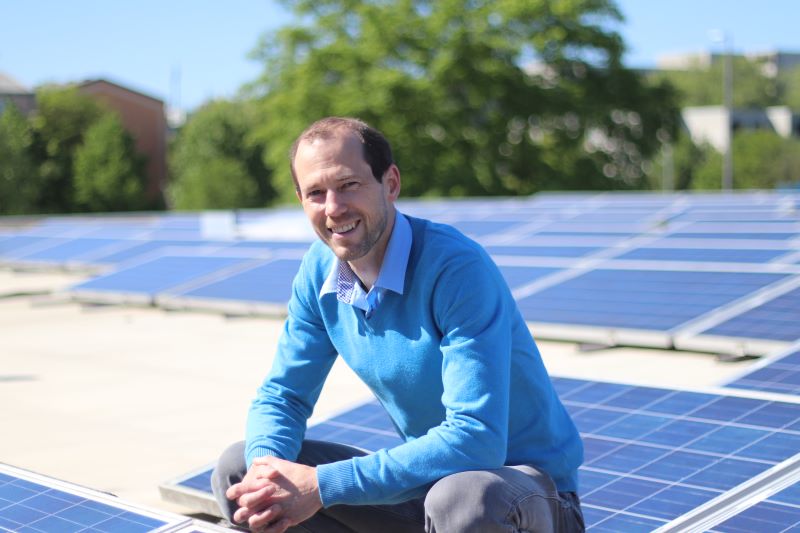 Installation-Gründer Meyer-Delpho lachend auf einem Dach mit Solarmodulen.