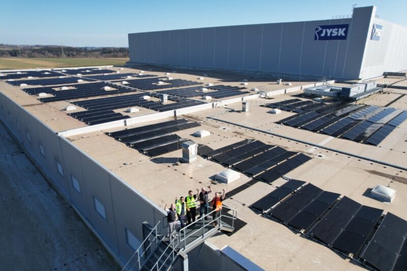 Dach eines Logistikgebäudes mit PV und winkenden Mitarbeitern.