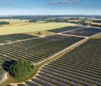 Luftbild zeigt Freiflächen-Solarpark umgeben von Äckern und Wiesen.