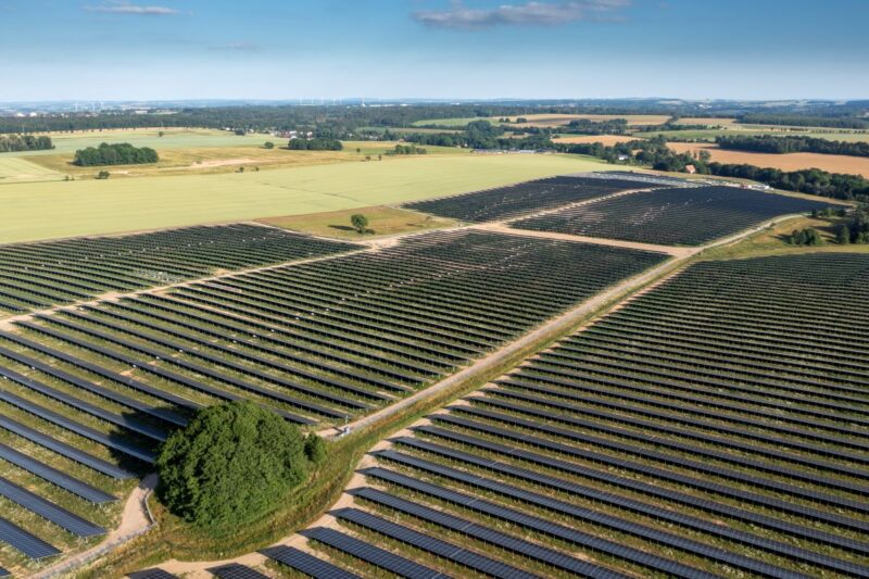 Luftbild zeigt Freiflächen-Solarpark umgeben von Äckern und Wiesen.