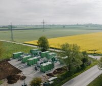 Luftbild von Batterie-Speicher-Projekt, zu sehen sind grüne Container und ein Rapsfeld.