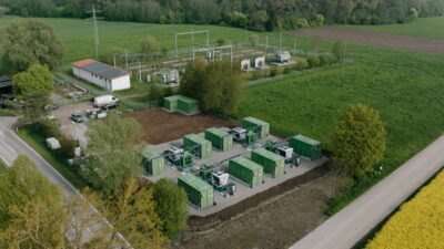 Luftbild zeigt Großspeicher mit zehn Batteriecontainern auf der grünen Wiese.