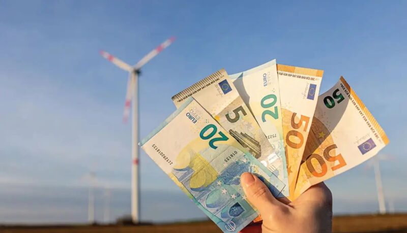Im Bild Geldscheine vor Windenergieanlage, das Windenergieanlagenabgabegesetz Brandenburg legt eine Sonderabgabe für Windräder fest.