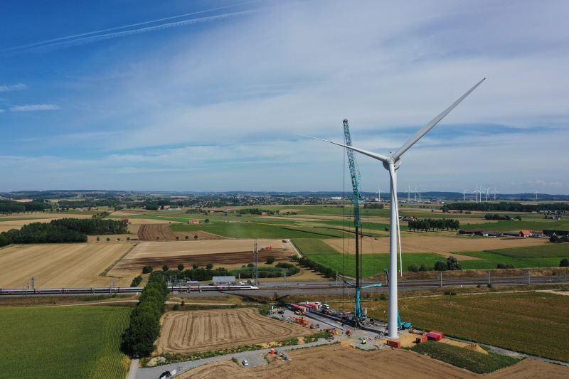 Eine Windkraftanlage während der Errichtung in einer flachen ländlichen Region mit Windpark am Horizont.