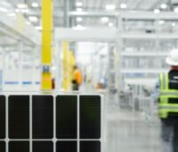 Innenansicht einer Modulfabrik mit Arbeiter im Hintergrund und blauen Solarmodulen vorne.