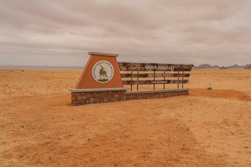 Flache Wüstenlandschaft mit Schild, das auf Nationalpark hinweist - Symbol für Wasserstoff- und Windenergiegewinnung in Namibia