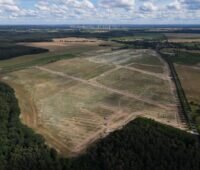 Luftbild zeigt eine vorbereitete Fläche zum Bau eines großen Freiflächen-Solarparks umgeben von Wäldchen und Feldern.