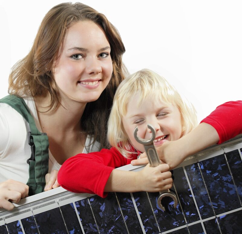 Im Bild eine junge Frau und ein Mädchen mit Photovoltaik-Modul und Schraubenschlüssel als Symbol für den Workshop Solar-Selbstbau für Frauen.