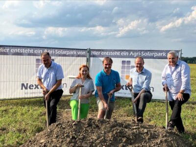 5 Personen vor einem Aufsteller zu Agri-PV beim Spatenstich auf dem Land.