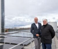 Zwei lachende Männer auf einem Hochhausdach mit PV-Anlage