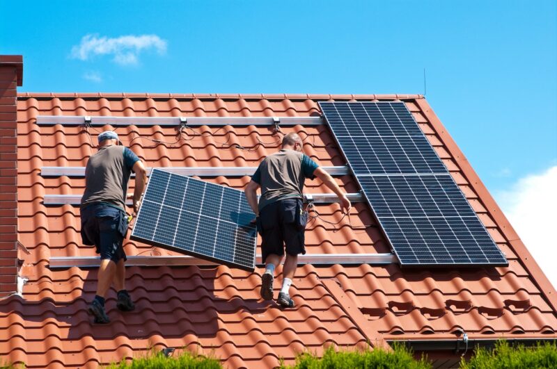 Zwei Männer tragen Photovoltaik-Modul auf Dach