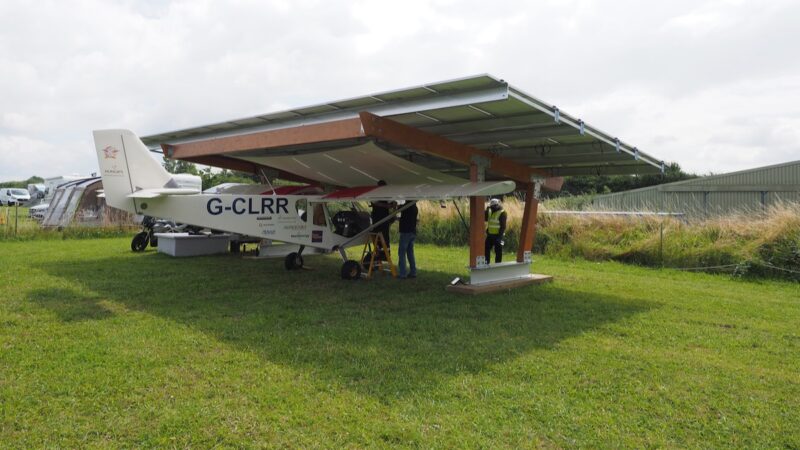 eine Art Photovoltaik-Carport auf einem grünen Rasen mit einem Leichtflugzeug darunter