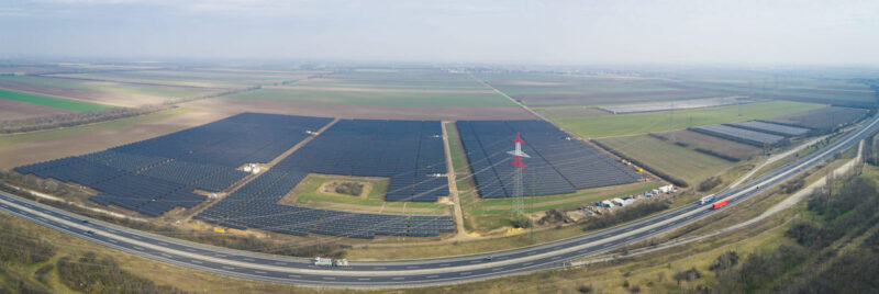 geschwungene Panorama-Aufnahme aus der Luft von einer Photovoltaik-Freiflächenanlage und Stromnetz in Österreich