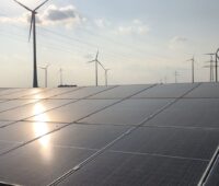 Photovoltaik mit refelktiernder Sonne im Vordergrund, dahinter Windkraftanlagen.