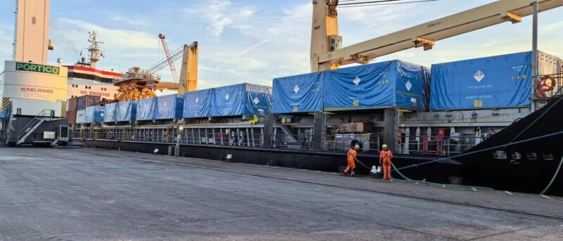 Ein Schiff an einer Kaikante, darauf Container gestapelt - Lieferung der Großspeicher Powertitan von Sungrow.