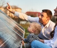 Im Bild Vater, Mutter und Kind mit Photovoltaik-Anlage, für die Qcells nun eine Versicherung mitliefert.