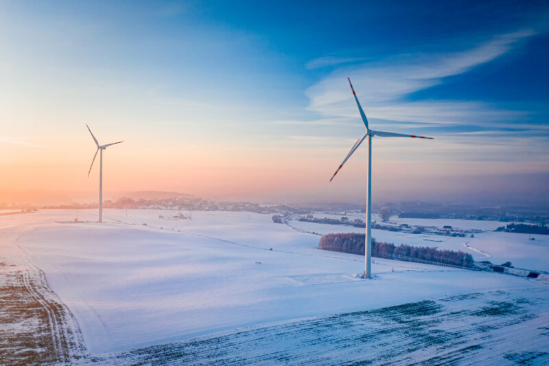 Windturbinen in einer flachen Winterlandschaft bei Sonnenuntergang.