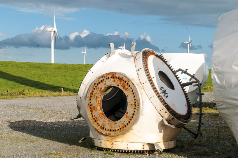 Windkraft-Repowering-Projekt in Nordfriesland. Im Hintergrund verschiedene Generationen von Windenergieanlagen und ein Nordseedeich. Im vordergrund die leicht angerostete Nabe einer demontierten Windenergieanlage.