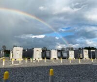 Eine Reihe von Containern mit Batteriespeichern vor wolkigem Himmel mit Regenbogen.