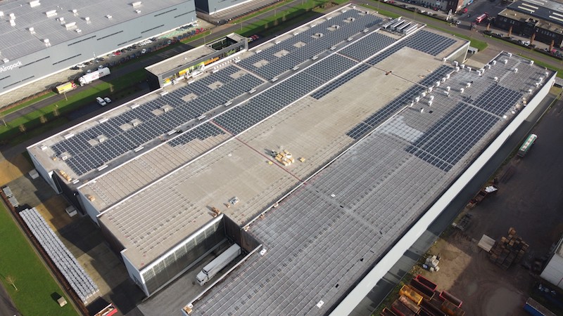 Das Dach eines Gewerbebetriebes wird eine Glas-Glas-Photovoltaikanlage installiert.. Es ist mit Gestellen belegt, auf denen die ersten dunklen Solarmodule installiert wurden.