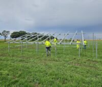 Arbeiter bauen auf grüner Wiese Montage-Gestell für Photovoltaik-Anlage auf.
