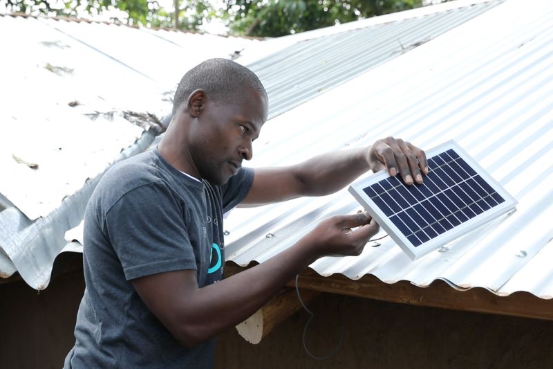 Ein Anwender prüft ein einzelner Solarmodul. Er steht vor Wellblechdächern.