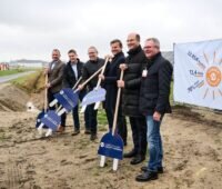 Menschen mit Grabwerkzeugen die aussehen wie Schuko-Stecker an Stöcken - Spatenstich am Flughafen Nürnberg für Solaranlage.