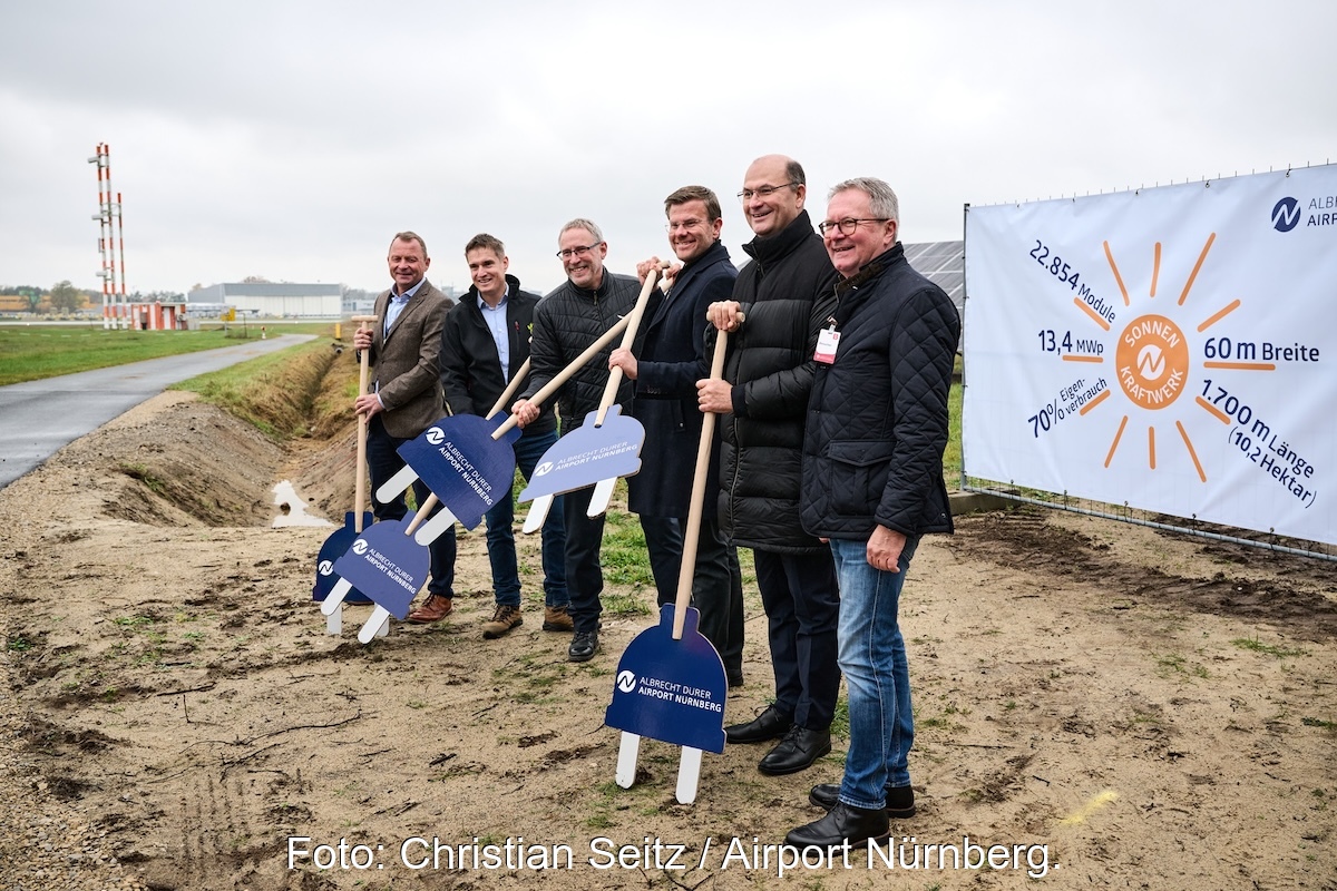 Menschen mit Grabwerkzeugen die aussehen wie Schuko-Stecker an Stöcken - Spatenstich am Flughafen Nürnberg für Solaranlage.