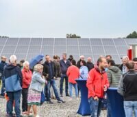 Menschen vor einer Freiflächen-Solaranlage, dabei ein Regenschirm.