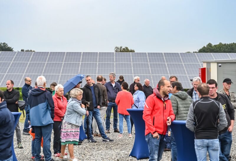 Menschen vor einer Freiflächen-Solaranlage, dabei ein Regenschirm.