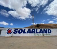 Schriftzug Solarland auf einer Mauer mit Sonne sowie einer Windkraftanlage im Hintergrund.