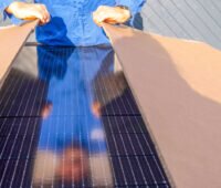 Arbeiter im Blaumann packt ein Solarpaket mit Photovoltaikmodulen aus