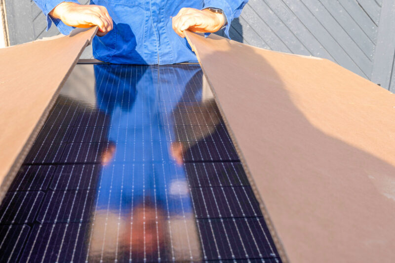 Arbeiter im Blaumann packt ein Solarpaket mit Photovoltaikmodulen aus