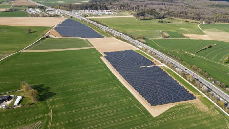 Luftbild eines Solarparks an der Landstrasse neben landwirtscatlichen Grünflächen.