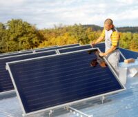 Ein Monteur installiert auf einem Flachdach Solarthermie-Kollektoren.
