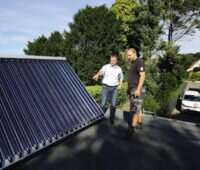 Zwei Personen im Gespräch auf einem Dach und betrachten dabei einen solarthermischen Kollektor