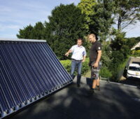Ein Monteuer bespricht sich auf dem Dach mit dem Eigentümer über die Installation von Solarkollektoren.