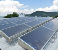 Auf einem Industriedach stehen Solarthermiekollektoren und ein Wasserspeicher. Im Hintergrund grüne Hügel.