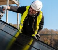 Im Bild ist ein Installateur, der PV-Module auf dem Dach befestigt. Laut Solarwatt-Marktstudie 2023 steigt das Interesse an der PV.