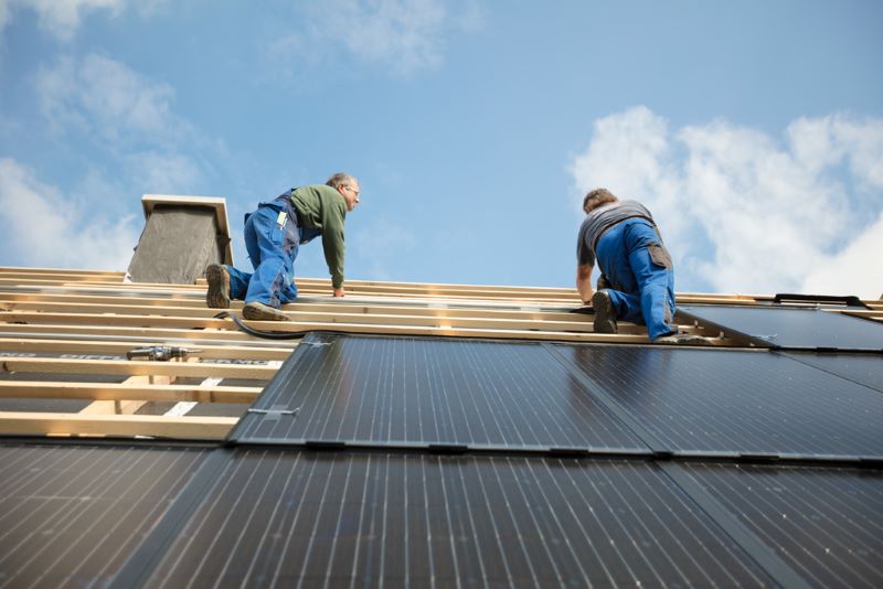 Zwei Arbeiter installieren PV-Module auf einem Spitzdach.