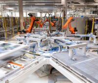 Blick in eine Photovoltaik-Produktion mit roten Roboterarmen und Modulen.