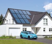 Das Bild zeigt ein großes Einfamilienhaus mit Photovoltaik-Anlage auf dem Dach und einem Elekotrauto vor dem Haus.